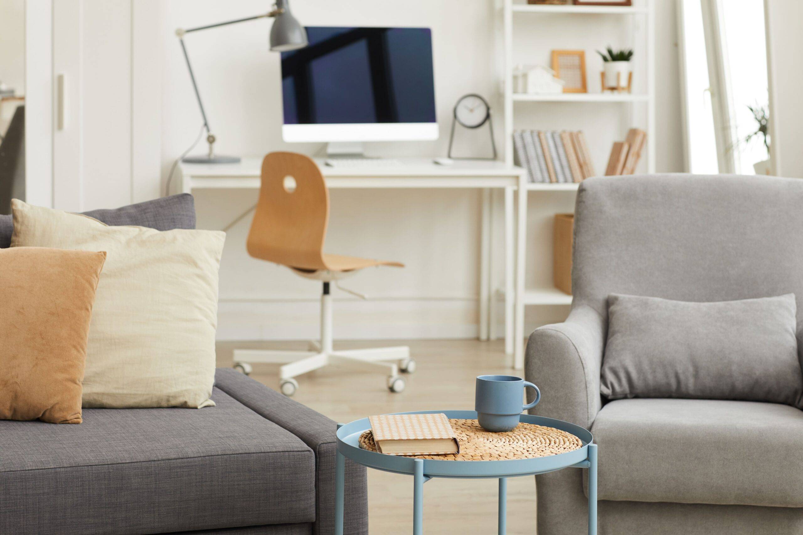 A minimalist living room design with a home office desk seen behind the couches.